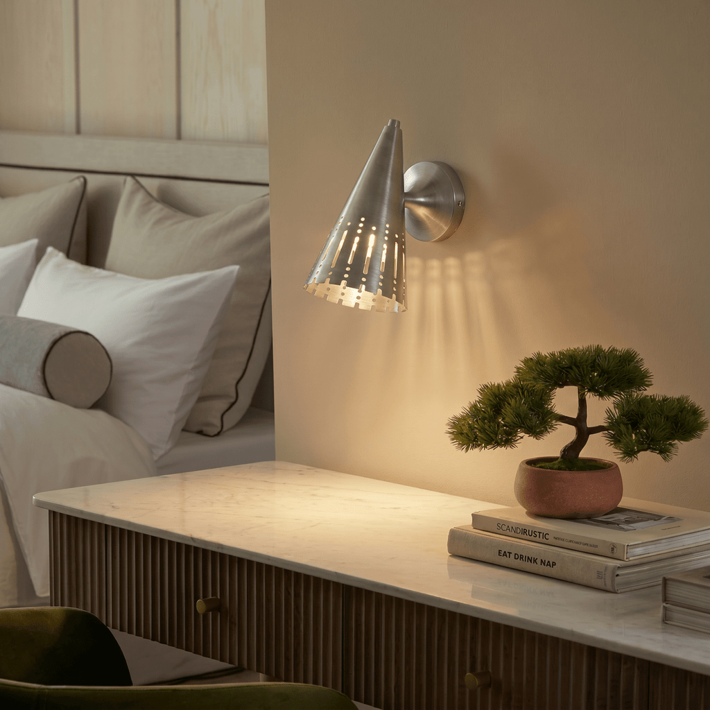 Clérachic wall lamp in chrome above a marble nightstand with a bonsai plant and stacked books.