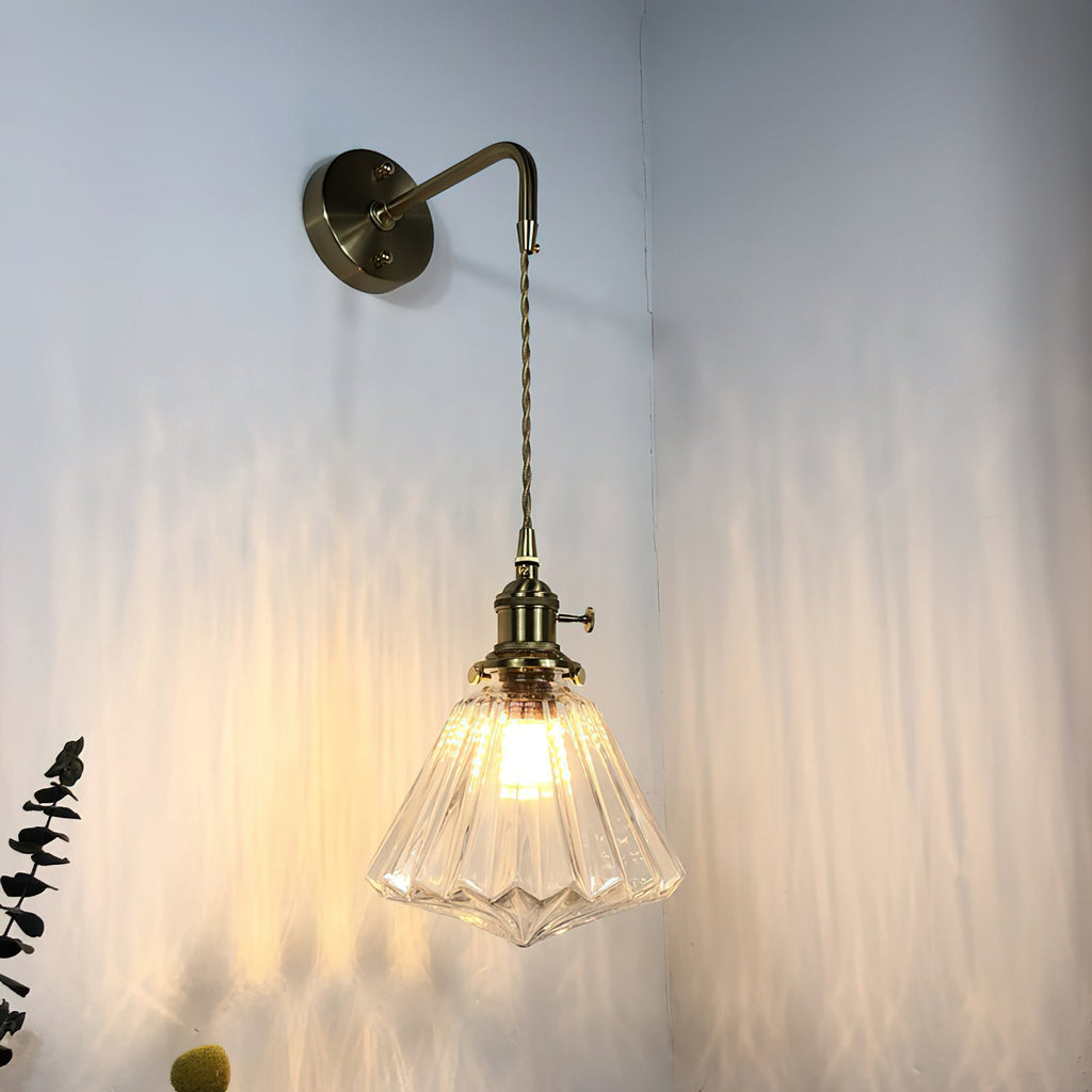 A Clérachic wall light in a darker, antique-bronze version, its ribbed glass shade lit and casting streaks on a pale wall.