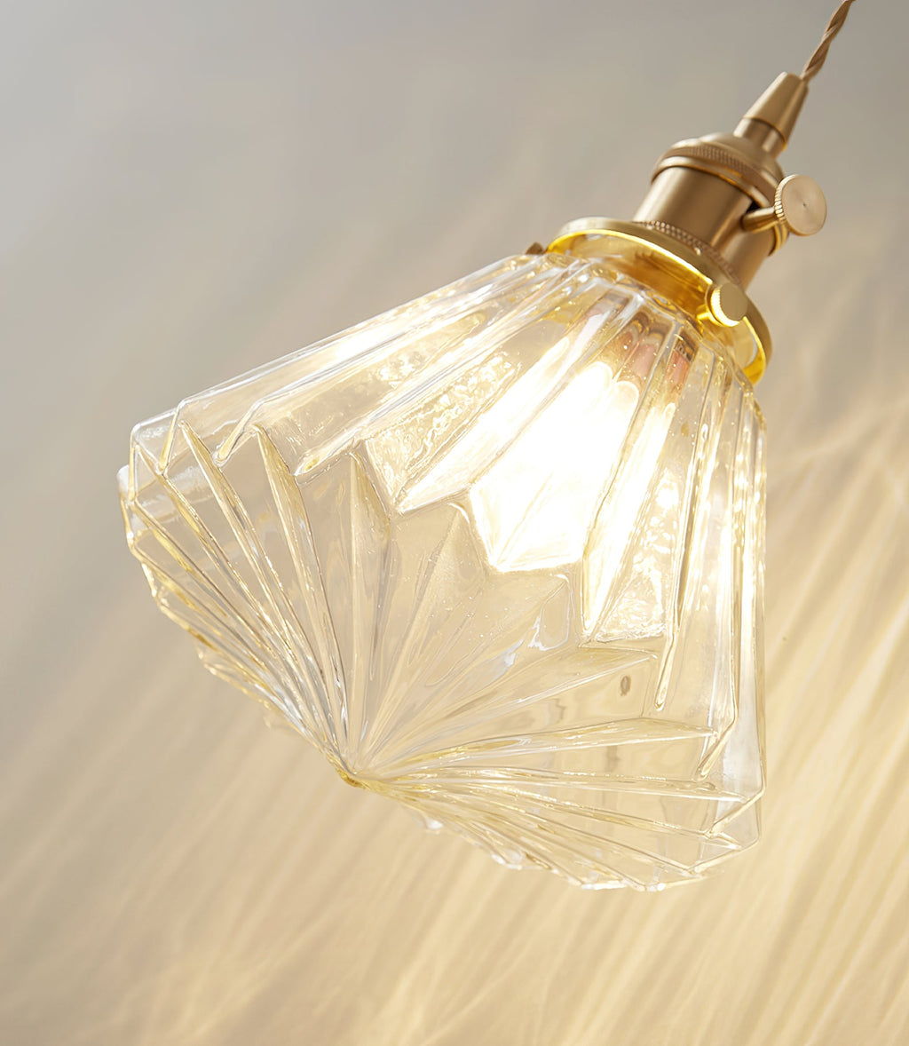 Close view of the faceted ribbed glass shade and brass socket on this Clérachic wall light, glowing warm.