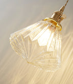 Close view of the faceted ribbed glass shade and brass socket on this Clérachic wall light, glowing warm.