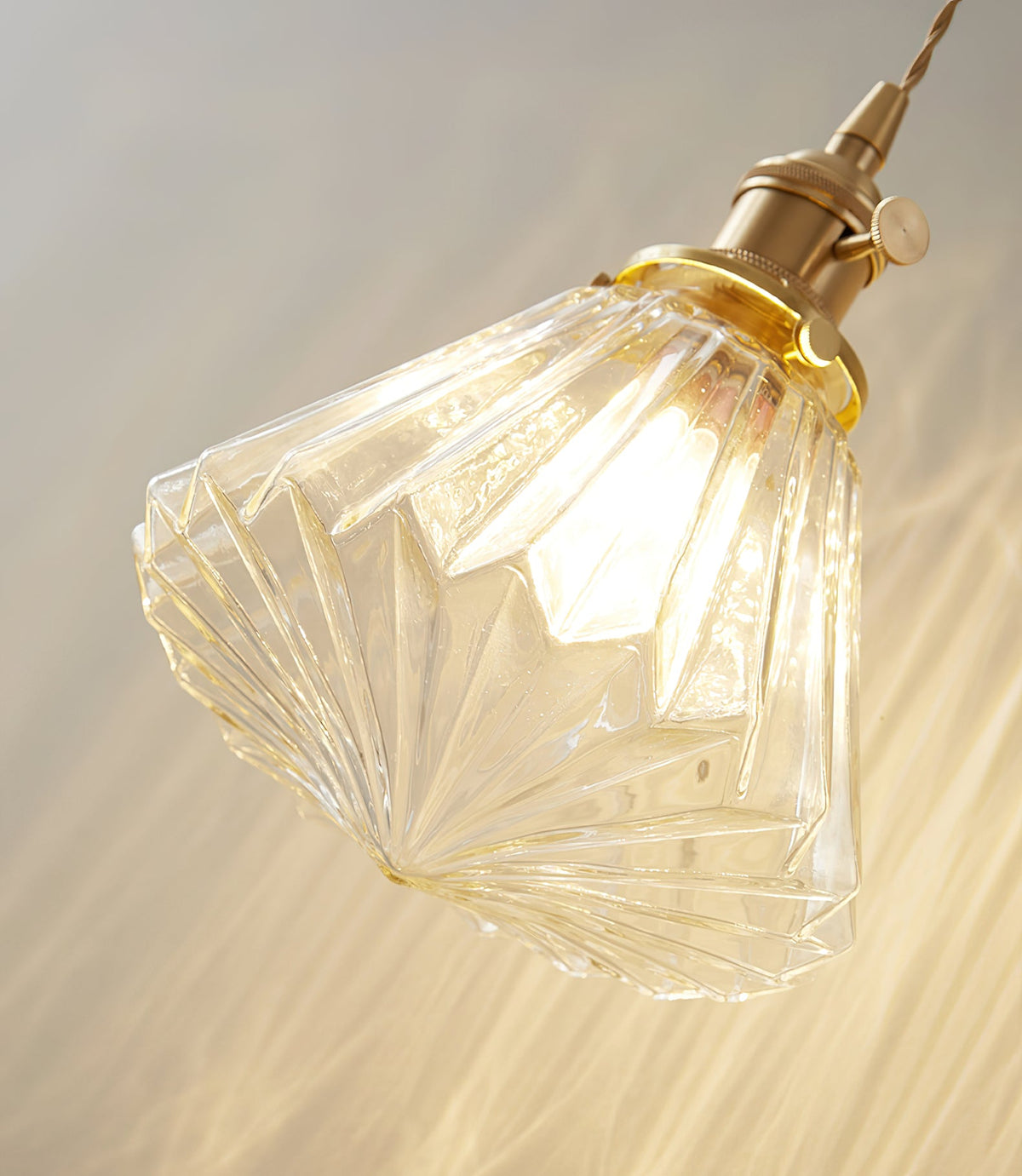 Close view of the faceted ribbed glass shade and brass socket on this Clérachic wall light, glowing warm.
