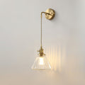 A Clérachic wall light lit on a light grey wall, its glass shade throwing vertical streaks of warm light to one side.