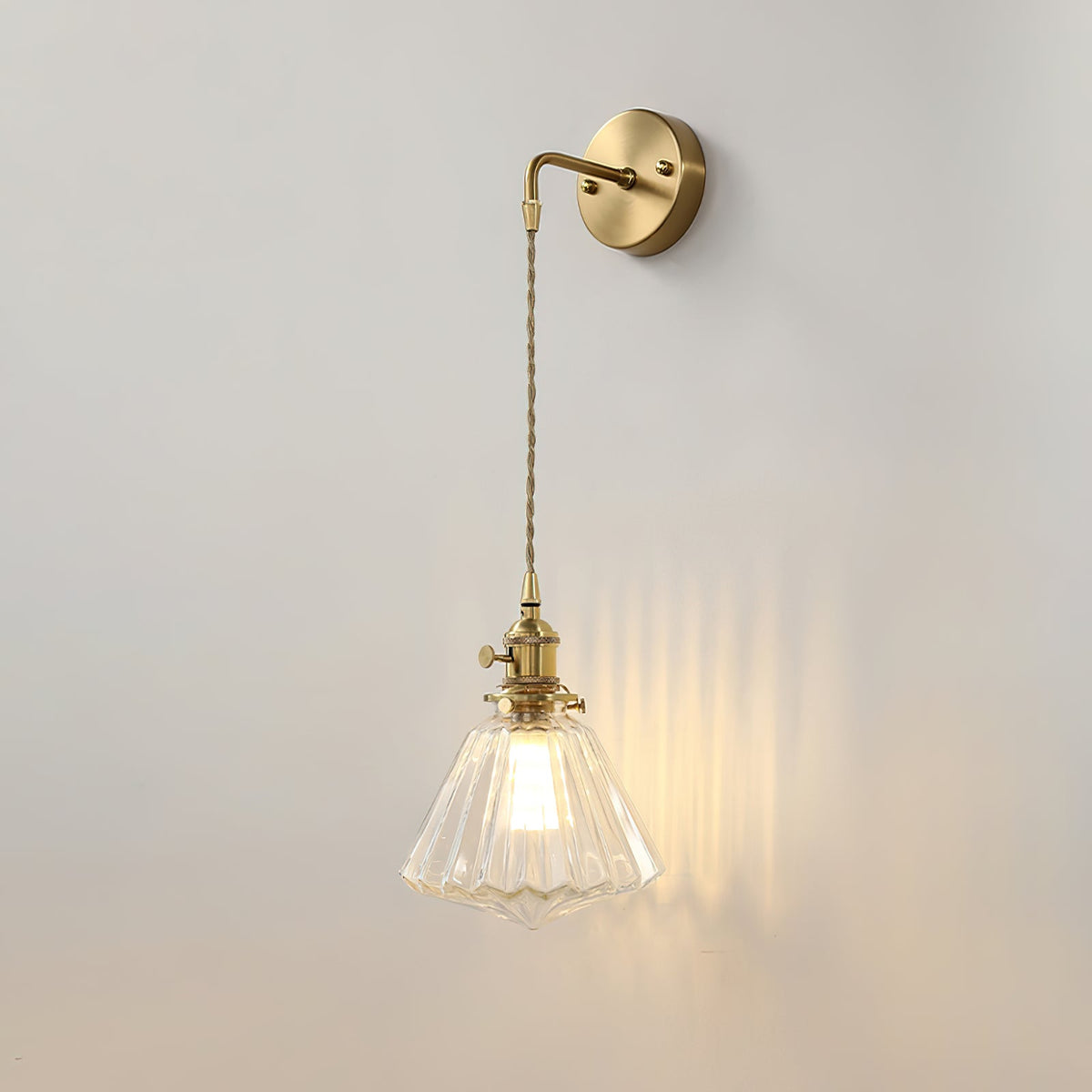 A Clérachic wall light lit on a light grey wall, its glass shade throwing vertical streaks of warm light to one side.