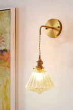 A Clérachic wall light on a peach-toned wall beside a framed abstract painting, its ribbed shade glowing amber.