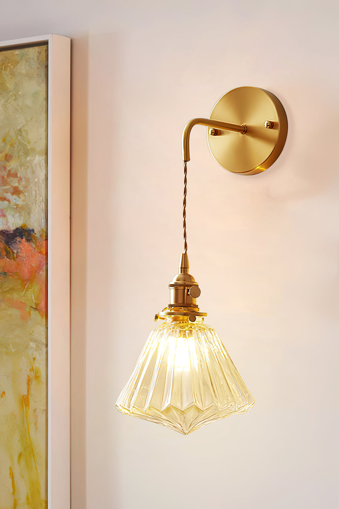 A Clérachic wall light on a peach-toned wall beside a framed abstract painting, its ribbed shade glowing amber.