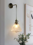 A Clérachic wall light in a darker bronze version, lit beside a framed line-art print and a vase of white flowers.