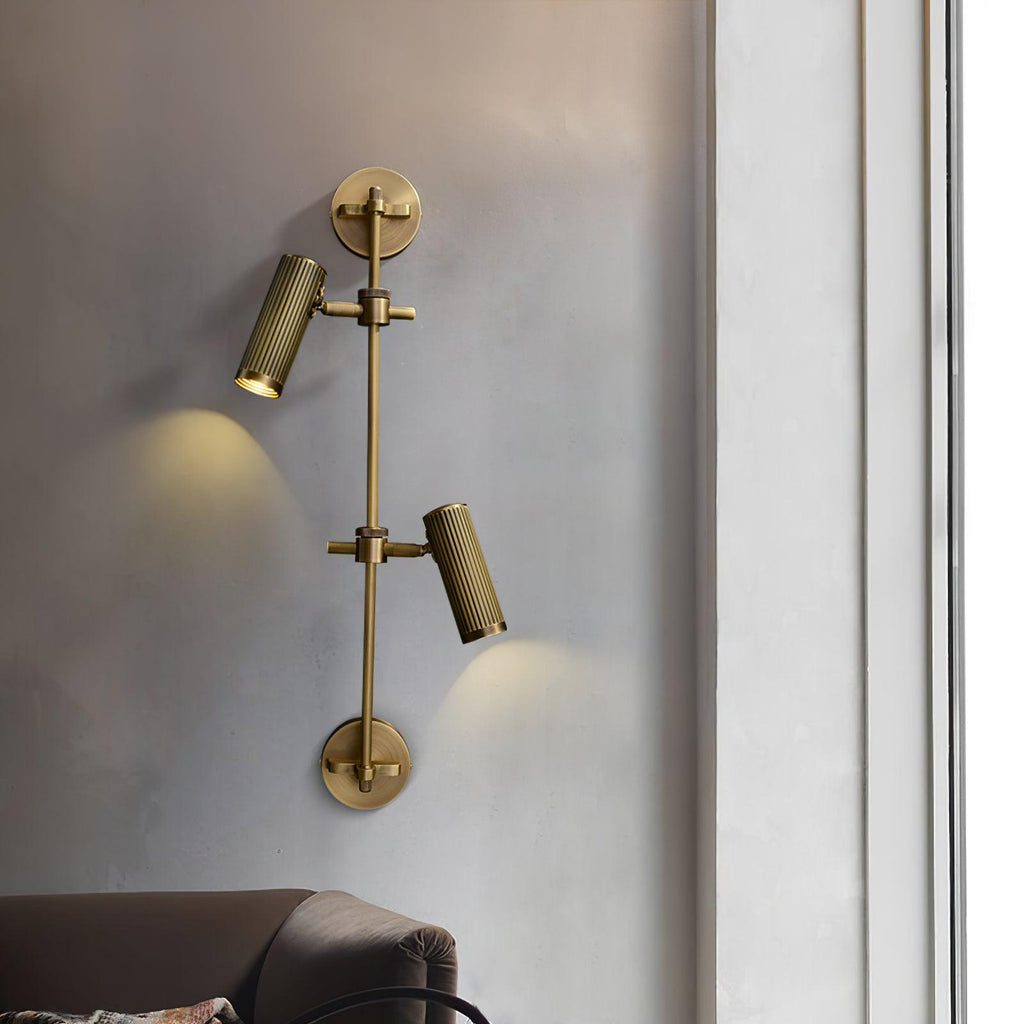 This Clérachic two-head wall light casts small pools of warm light down a grey wall, above the arm of a leather sofa.