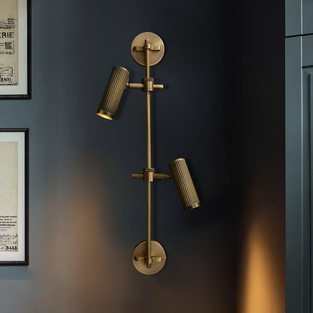 Two fluted bronze heads on a vertical rail from Clérachic, with warm light on a dark wall beside framed prints.