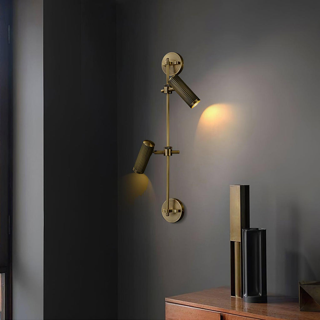 Clérachic wall light with one head tilted up and one aimed down, casting a warm glow on a grey wall beside a dark sideboard.