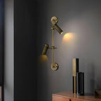 Clérachic wall light with one head tilted up and one aimed down, casting a warm glow on a grey wall beside a dark sideboard.