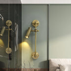 Clérachic wall light with one head, lit, on a sage-green wall beside a glass door that reflects a second light.