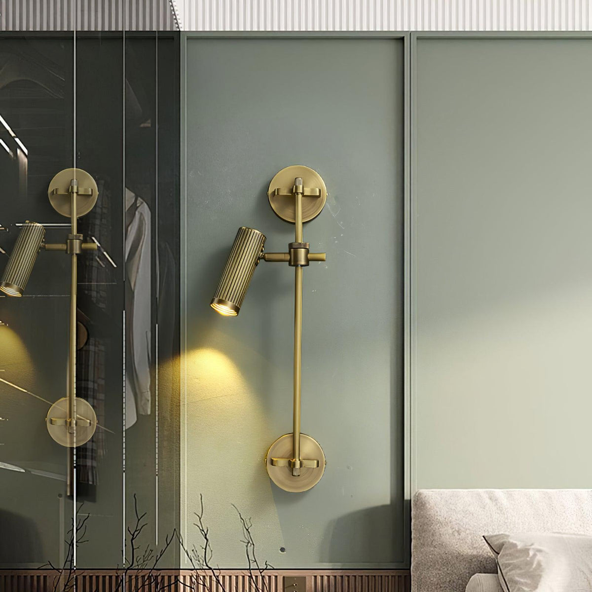 Clérachic wall light with one head, lit, on a sage-green wall beside a glass door that reflects a second light.