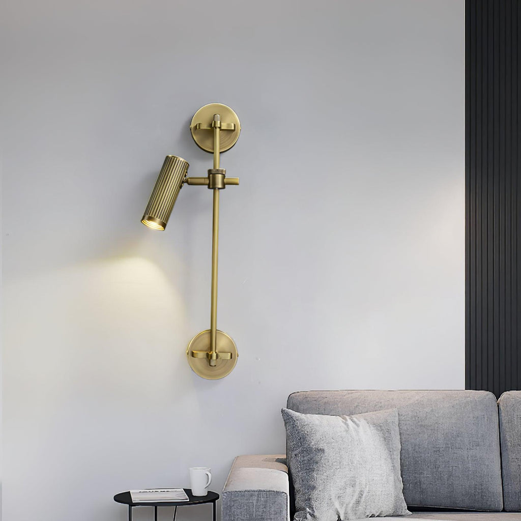 A single lit spot head on a bronze rail, from Clérachic, mounted on a pale wall above a grey sofa with a small black side table.