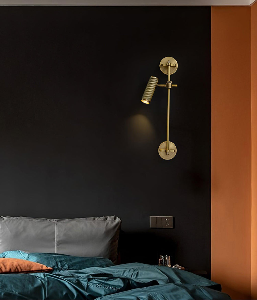 Clérachic wall light with a single lit head, mounted on a dark wall beside an orange panel, above a bed with teal bedding.