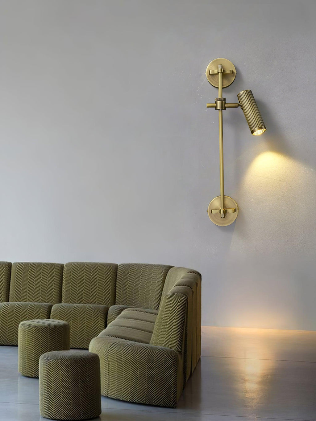A single bronze head on a slim rail, from Clérachic, lit on a pale grey wall above a green modular sofa and low stools.