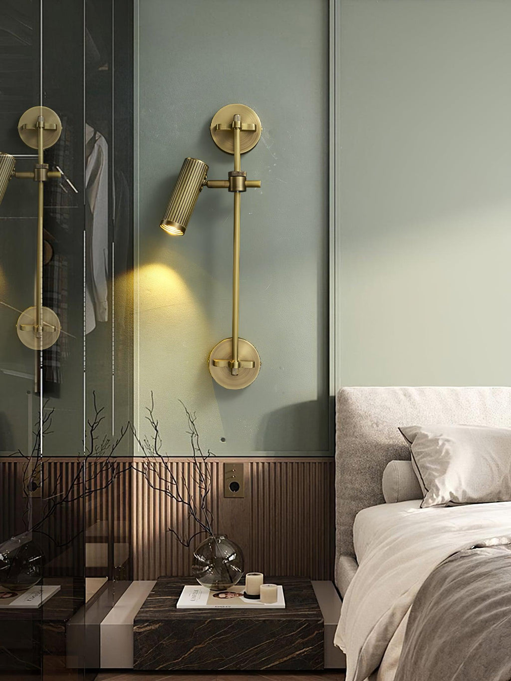 Clérachic wall light with one lit head on a sage-green wall, beside a glass wardrobe door and a bed with white linen.