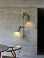 Two-head Clérachic wall light, lit, on a concrete-effect wall above a round dark table and a wooden chair.