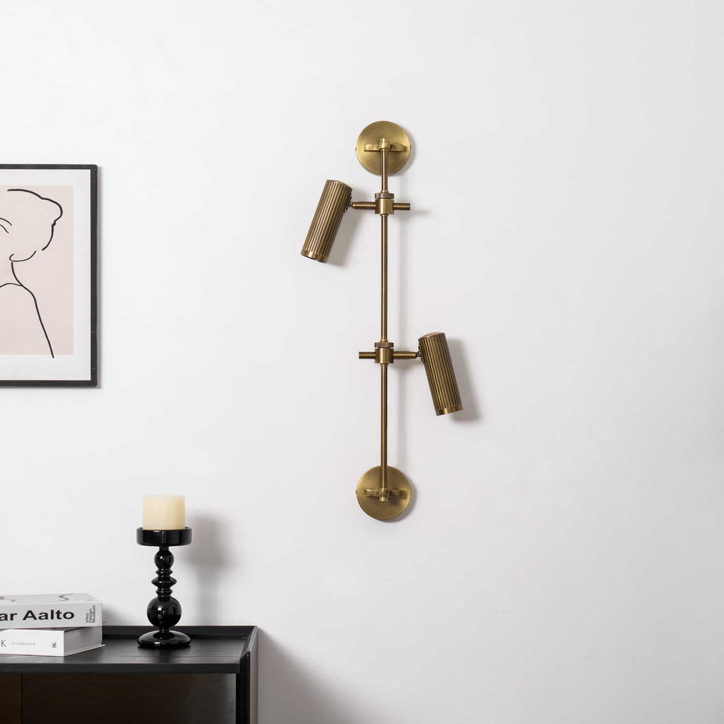 Two-head wall light from Clérachic in bronze, unlit, on a white wall with a framed line drawing and a candle on a dark table.