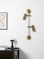 Bronze wall light with two heads from Clérachic, unlit, on a white wall above a dark sideboard with a black candlestick.