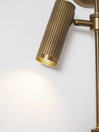 Close view of a fluted bronze head on this Clérachic wall light, lit, with a soft round pool of light on the wall below.