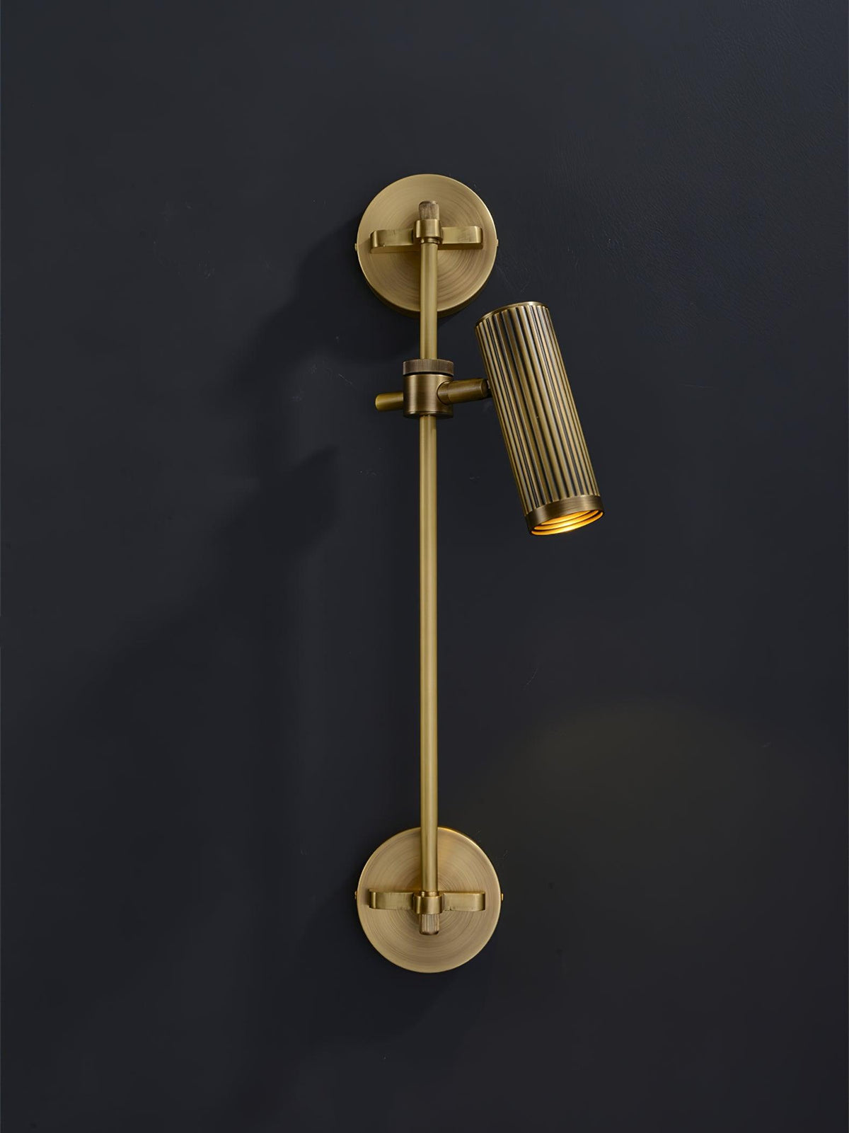 One fluted bronze head on a slim vertical rail from Clérachic, angled out from a dark wall with a faint glow below.