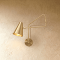 Clérachic wall lamp in brushed brass, a cone shade on an articulated swing arm against plaster.