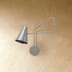 Clérachic wall lamp in chrome shown close, the jointed arm angled toward the polished cone shade.