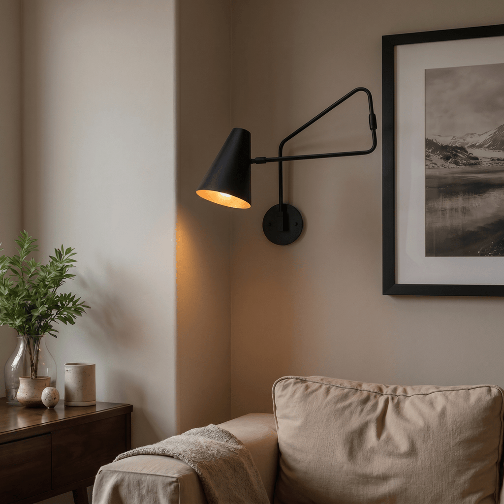 Clérachic wall lamp in matte black lighting a living room corner beside a sofa and a leafy plant.