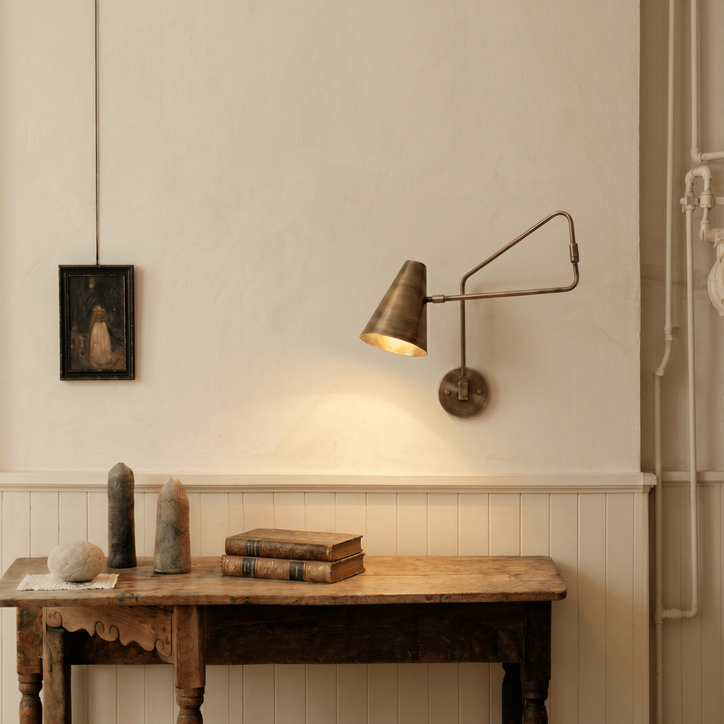 Clérachic wall lamp in vintage brass above a rustic console table with old books and a framed portrait.