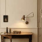 Clérachic wall lamp in vintage brass above a rustic console table with old books and a framed portrait.