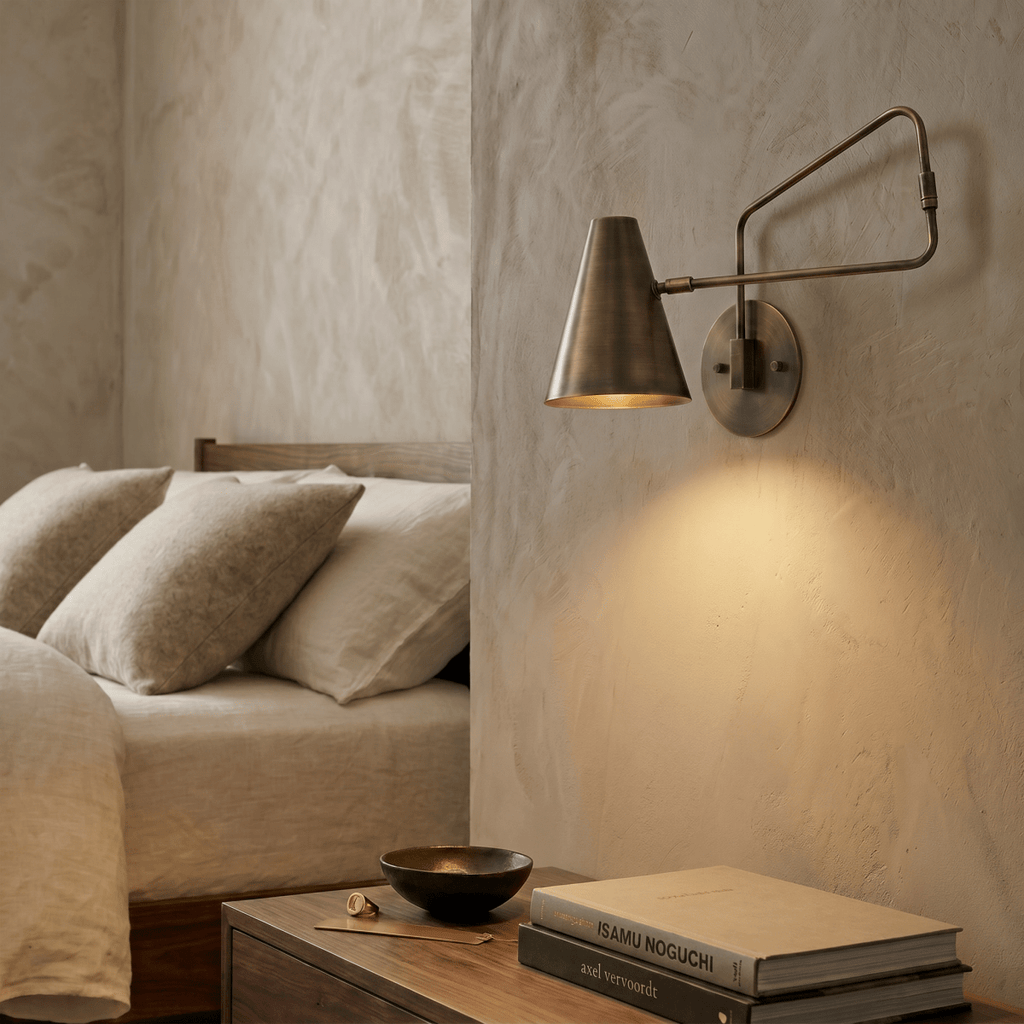 Clérachic wall lamp in vintage brass above a nightstand with stacked design books beside the bed.