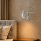 Clérachic wall lamp in chrome above a tufted headboard, its swing arm reaching over the nightstand.
