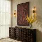 Pair of Clérachic brass and crystal wall lamps either side of a framed painting above a carved dark wood sideboard.