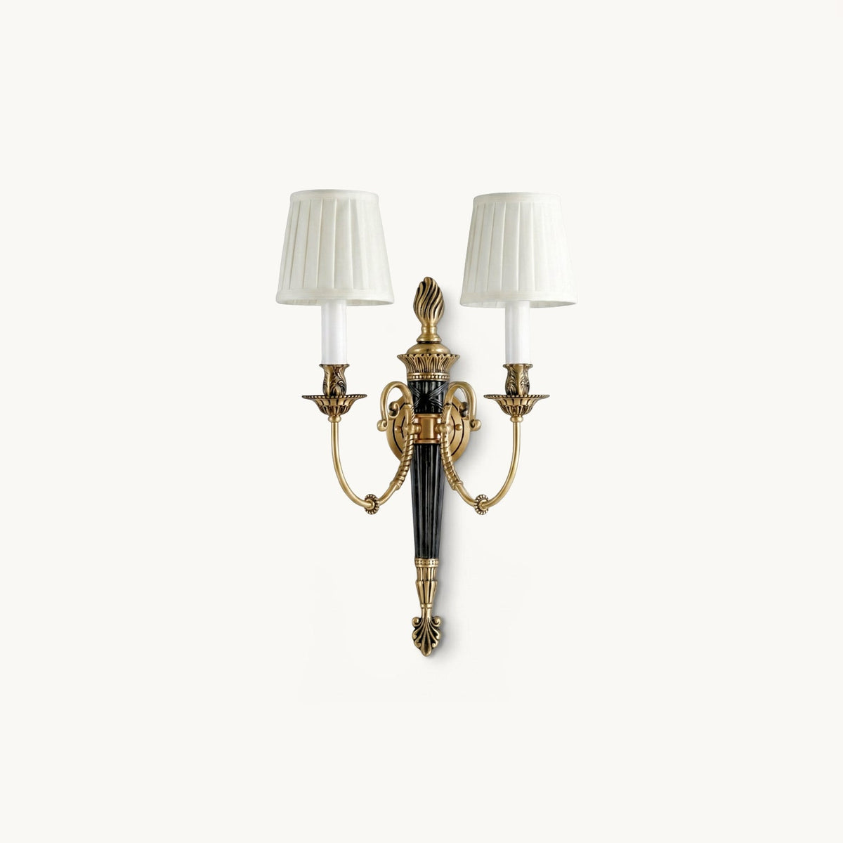 Two pleated white shades on antique brass arms and a black tapered column, this Clérachic wall light on a plain white backdrop.