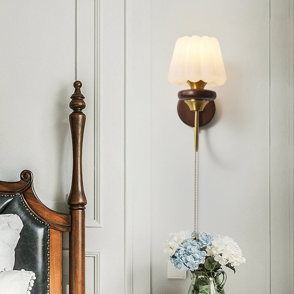 Fluted-shade Clérachic wall light above a bedside table with blue hydrangeas, next to a carved dark wood bedpost.