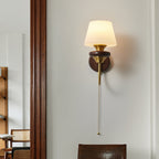 Another view of the tapered-shade Clérachic wall light beside a dark door frame, its pull chain hanging down the wall.