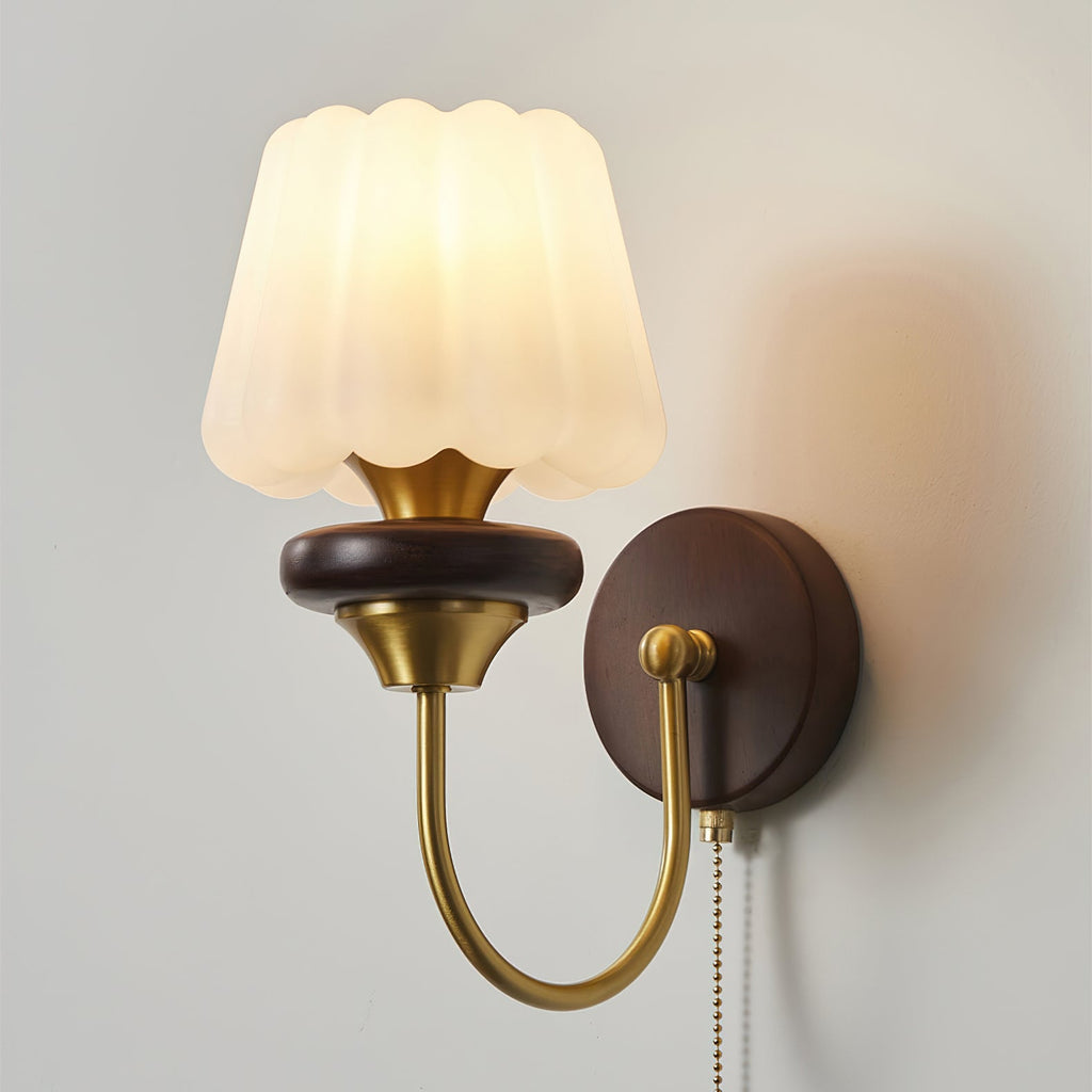 Lit, the fluted glass shade of this Clérachic wall lamp glows warm above its walnut ring and curved brass arm.