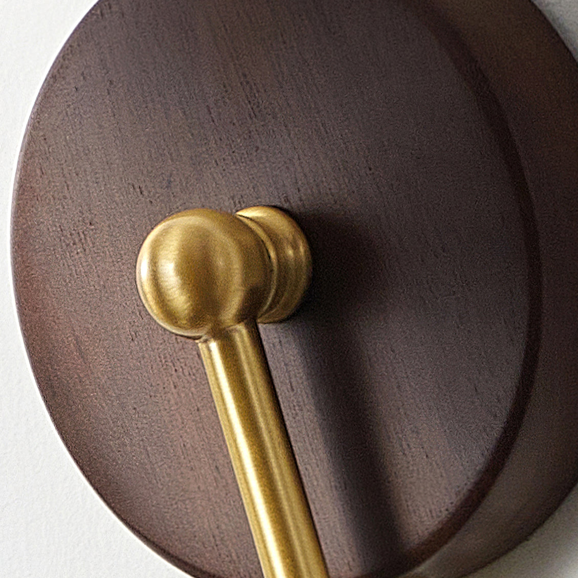 Close view of the round walnut backplate and the brass ball joint where the arm of this Clérachic wall lamp meets it.