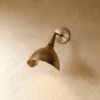 Clérachic wall lamp in vintage brass, a swiveling cone shade angled downward on a plaster wall.