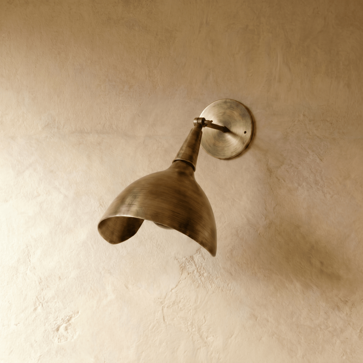 Clérachic wall lamp in vintage brass shown from another angle, its brushed cone shade catching warm light.
