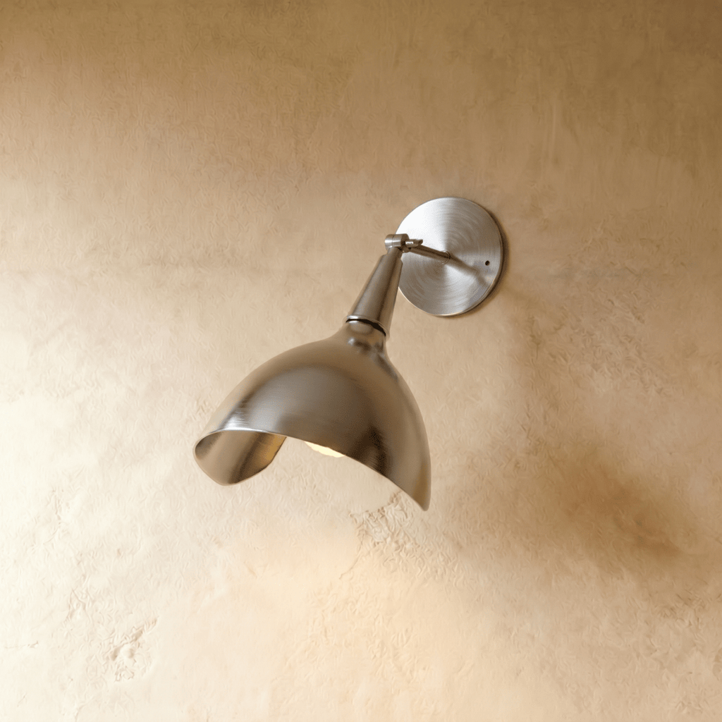 Clérachic wall lamp in chrome, its polished cone shade angled downward against a plaster wall.