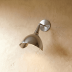 Clérachic wall lamp in chrome, its polished cone shade angled downward against a plaster wall.