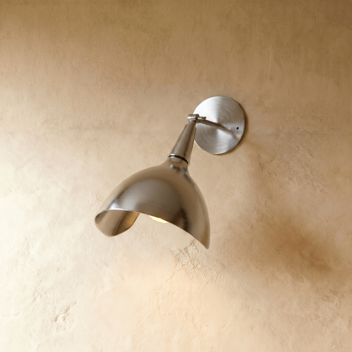 Clérachic wall lamp in chrome, its polished cone shade angled downward against a plaster wall.