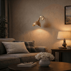 Clérachic wall lamp in brushed brass lighting a living room reading corner beside a sofa and table lamp.