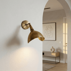 Clérachic wall lamp in vintage brass mounted by an archway leading into a bright entry hall.