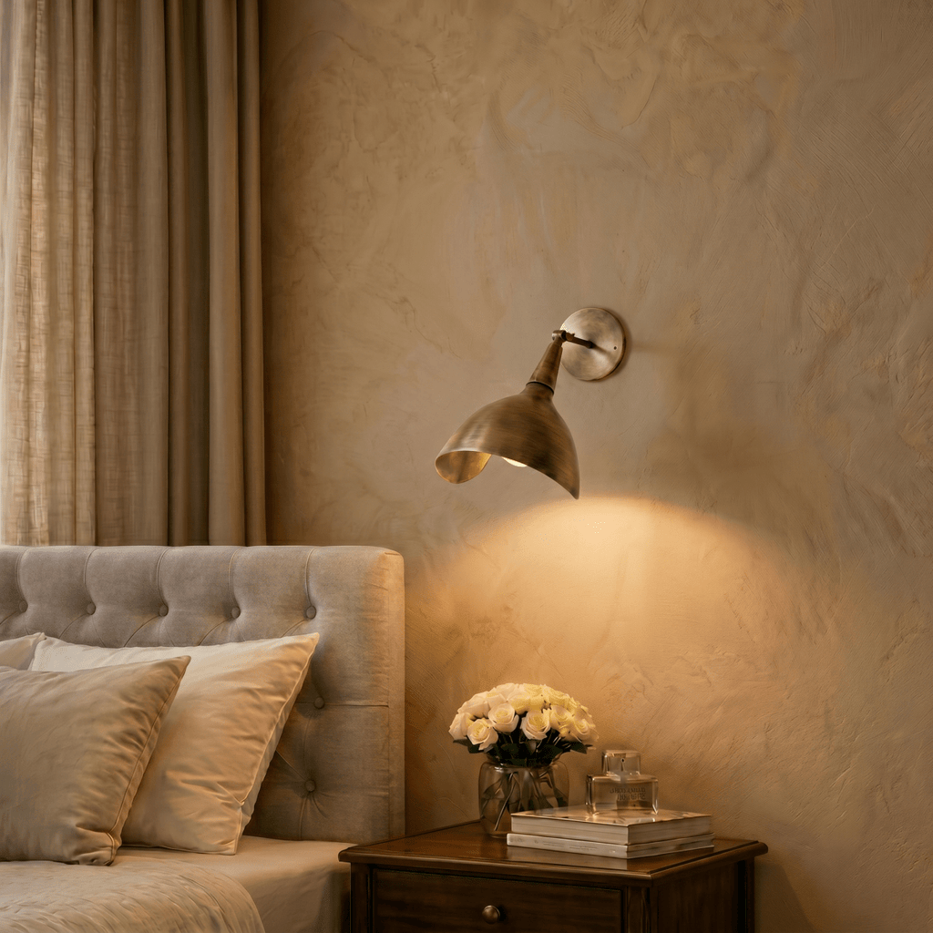 Clérachic wall lamp in vintage brass above a bedside table with white roses and stacked books.