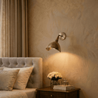 Clérachic wall lamp in vintage brass above a bedside table with white roses and stacked books.