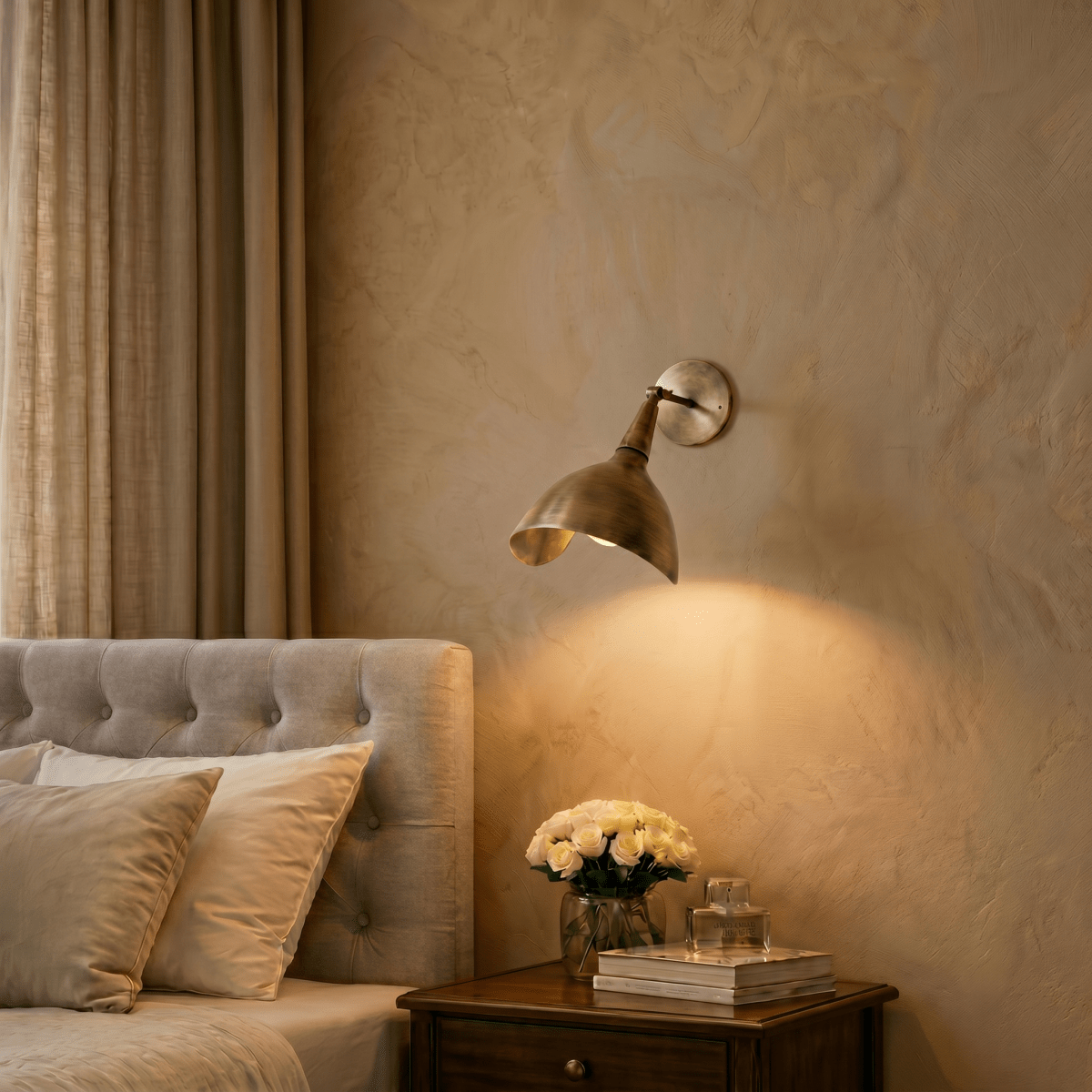Clérachic wall lamp in vintage brass above a bedside table with white roses and stacked books.