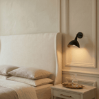 Clérachic wall lamp in matte black above a marble nightstand with a glass carafe on a brass tray.