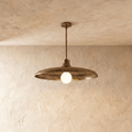 Clérachic pendant light in vintage brass, its wide disc shade and opal glass bulb hung from a plaster ceiling.
